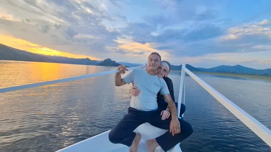 A couple sitting together on the bow as the sun sets over the lake