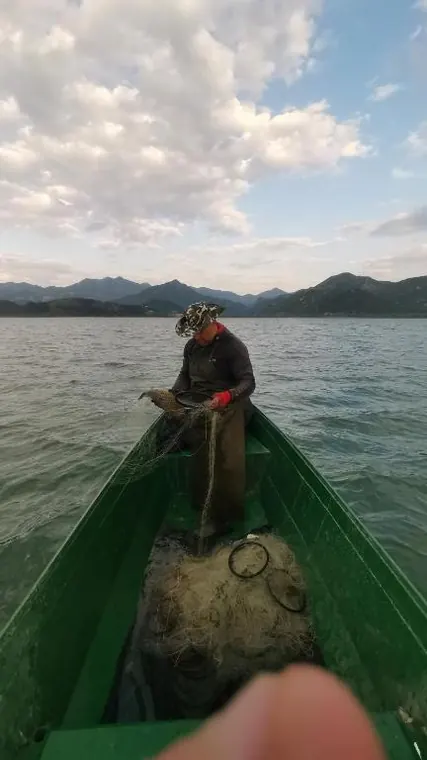 A fisherman pulling nets from a traditional wooden boat